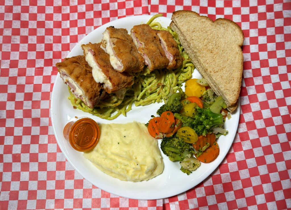 Cordon Bleu over a green pasta, mashed potatoes, steamed veggies, and toast