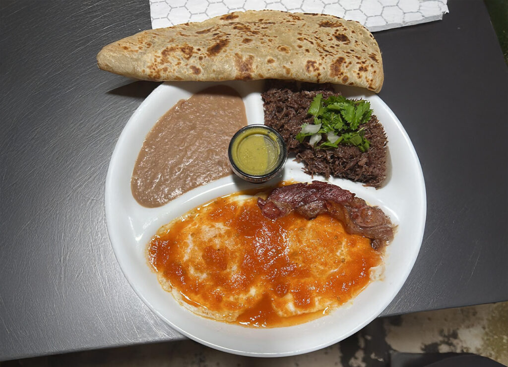 Eggs in salsa with bacon, refried beans, barbacoa, and a flour tortilla