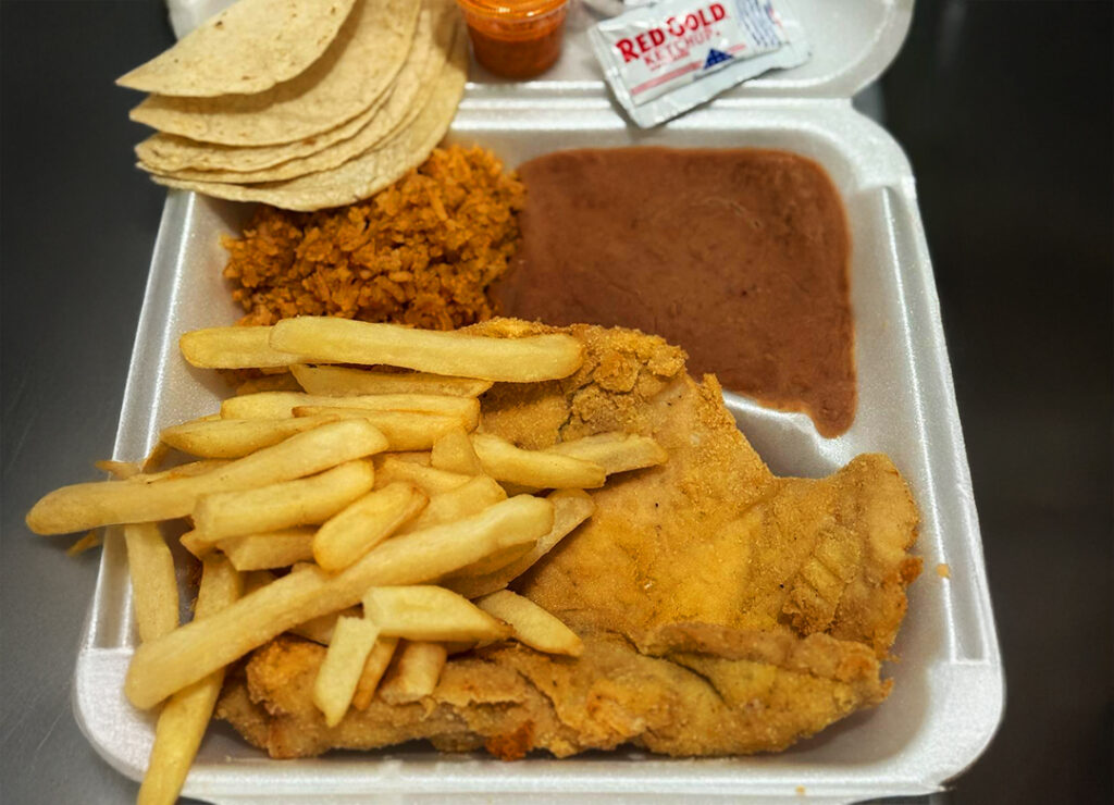 To-go plate of chicken milanesa, fries, rice, refried beans, and corn tortillas